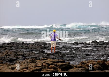 Homme mûr solitaire pêchant avec canne à pêche sur le rivage volcanique rocheux, Fuerteventura, îles Canaries, Espagne. Prise en novembre 2024 Banque D'Images