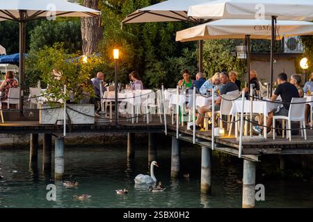 Sirmione, Italie - Sep 21st, 2024 : les gens apprécient de manger au bord du lac comme un cygne flotte à travers le lac de Garde Banque D'Images