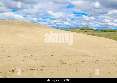 Colline de sable avec un ciel nuageux en arrière-plan. Le ciel est principalement bleu avec quelques nuages Banque D'Images