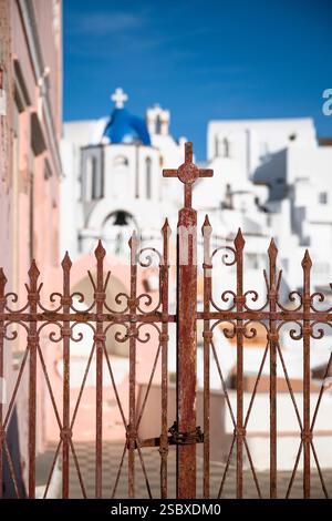 Porte d'entrée en fer forgé rouillé devant des maisons blanches et une église avec un dôme bleu à Oia. Santorin, Grèce Banque D'Images