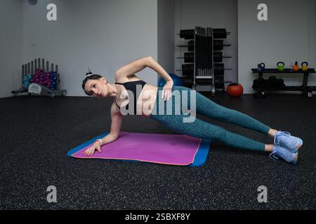 Jeune femme s'engageant dans un exercice de planche latérale sur un tapis de yoga dans un gymnase, mettant en valeur la force et l'équilibre tout en se concentrant sur la stabilité du tronc et sural Banque D'Images