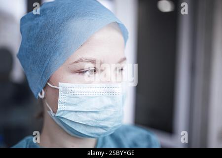 Vue de profil d'une personne dans des gommages bleus et un masque, semblant réfléchi à l'intérieur Banque D'Images