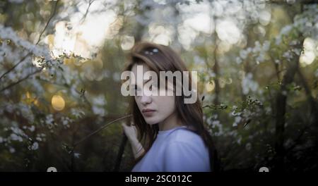 Femme regardant directement la caméra dans un cadre naturel avec des fleurs printanières et une ambiance nocturne Banque D'Images