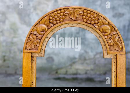 Motif raisin et feuilles complexes sculpté sur un dossier de chaise en bois, mettant en valeur un savoir-faire artisanal sur un fond naturel flou. Banque D'Images
