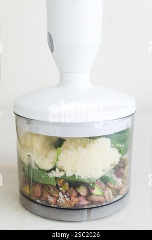 Pistaches rôties au basilic, à l'ail et au fromage râpé dans un bol de mixeur. Le processus de fabrication du pesto de pistache. Orientation verticale. Focales sélectives Banque D'Images