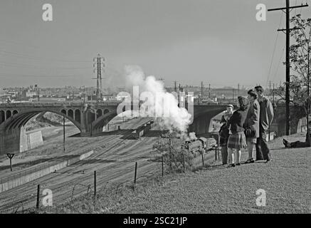 La vue par temps clair regardant vers le sud à partir d'Elysian Park à travers les lignes de chemin de fer de fret et la rivière Los Angeles, LA, Californie, États-Unis c. les années 1950 Une locomotive à vapeur tirant des wagons de marchandises est en dessous. Le North Broadway Bridge traverse la rivière et les pistes. Ceci est tiré du négatif d’un vieux photographe amateur noir et blanc – une photographie vintage des années 1950/60. Banque D'Images