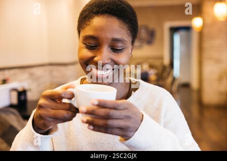 Femme tenant une tasse, profitant d'une boisson chaude à l'intérieur Banque D'Images