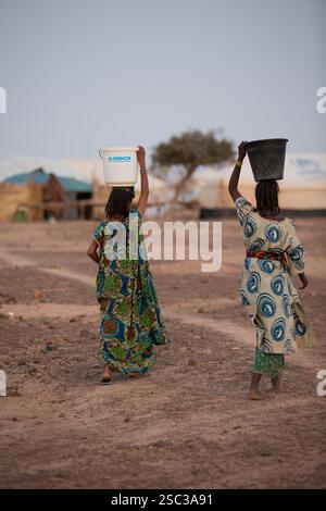Camp de réfugiés maliens de Mentao, près de Gibo, dans le nord du Burkina Faso mai 2012 : des femmes touaregs vont chercher de l'eau dans une pompe à eau manuelle du camp. Jusqu'à présent, l'aide alimentaire et autre est insuffisante pour ces réfugiés. Les réfugiés, pour la plupart Touregs, sont aujourd’hui plus de 60 000 au Burkina Faso seulement, et continuent d’arriver quotidiennement dans les camps, suite au chaos politique créé par le coup d’État malien le 22 mars 2012. Photographie de Mike Goldwater Banque D'Images