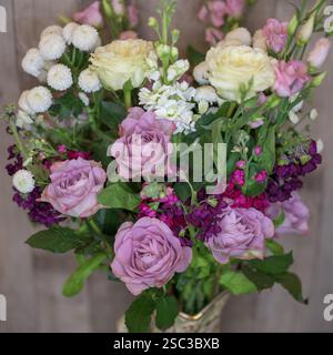 Un bel arrangement de fleurs mélangées mettant en valeur des roses de différentes couleurs dans un vase décoratif sur un fond neutre Banque D'Images
