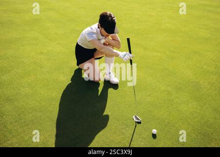 Gros plan d'une golfeuse accroupie, visant un putt sur un terrain de golf vert, concentrée et déterminée. Banque D'Images