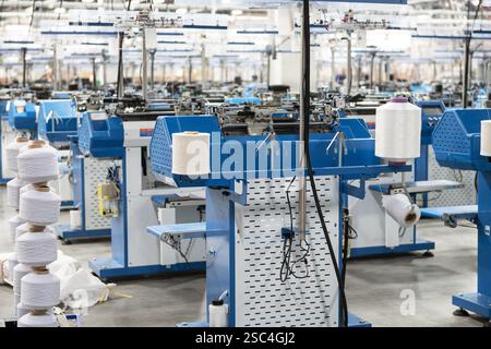 Vue de machines automatisées de fabrication de textiles dans une usine, avec des bobines de fil blanc prêtes pour le traitement. Banque D'Images