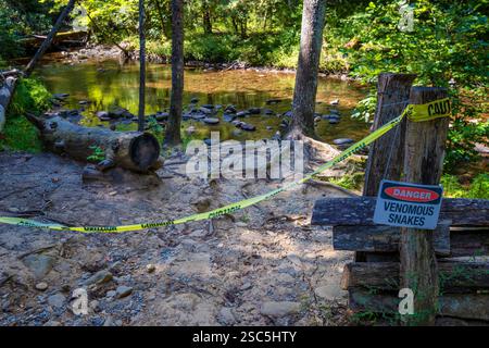 Ruban d'avertissement jaune et panneau de danger près du bord de l'eau avertissant les visiteurs de Cade Cove de serpents venimeux. Banque D'Images