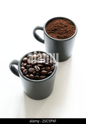 Deux tasses à café grises avec des grains de café et du café moulu isolé sur fond blanc. Vue de dessus. Copier l'espace. Banque D'Images