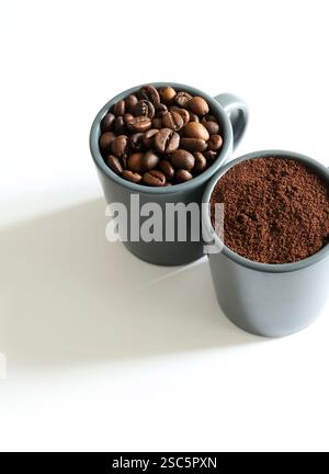 Deux tasses à café grises avec des grains de café et du café moulu isolé sur fond blanc. Vue de dessus. Copier l'espace. Banque D'Images
