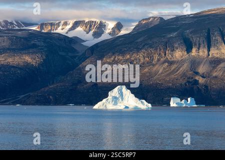 Icebergs flottant dans la lumière du matin au large de la côte voisine avec des montagnes abruptes couvertes de glaciers. Fjord d'Uummannaq, Groenland, Danemark, Amérique du Nord Banque D'Images