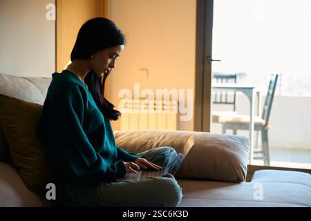 Jeune femme concentrée travaillant à distance à partir du bureau à domicile en utilisant un ordinateur portable sur le canapé Banque D'Images