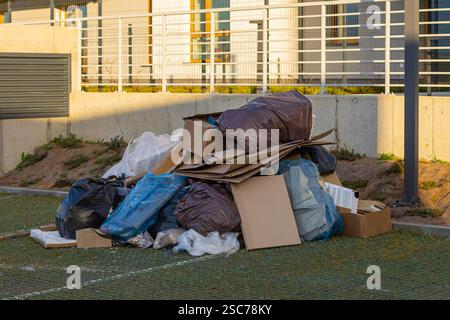 Pile de déchets mélangés avec des sacs en plastique noirs et bleus, des boîtes en carton jetées près d'un quartier résidentiel moderne. Pollution urbaine et élimination des déchets Banque D'Images