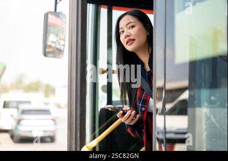 Une femme asiatique insouciante et positive descend du bus à un arrêt de bus, arrivant à destination tout en voyageant par les transports en commun dans la ville. personnes a Banque D'Images