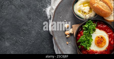 Oeufs Shakshuka dans une casserole avec du pain sur un fond sombre. Oeufs pochés dans une sauce épicée au poivre tomate. Œufs brouillés juifs traditionnels. Vue de dessus. PA Banque D'Images