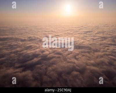 Une vue aérienne à couper le souffle du lever du soleil au-dessus d'une vaste mer de nuages. La lumière dorée projette une lueur douce sur la brume roulante, créant un rêve, tranquille Banque D'Images