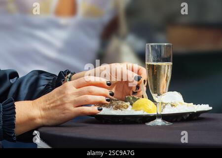 Une image en gros plan montrant les mains d'une femme appréciant un plat gastronomique d'huîtres accompagné d'un verre de vin, incarnant luxe et élégance., style, et c Banque D'Images