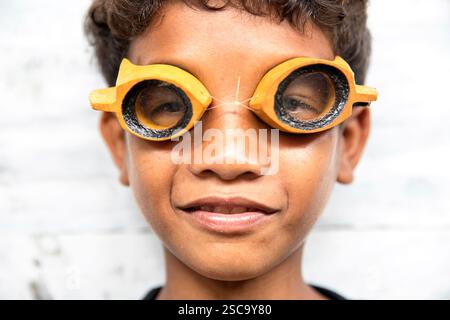 Portrait en gros plan d'un garçon Bajau local portant des lunettes de plongée en bois fabriquées à la main, illustrant le style de vie authentique des gitans de la mer à Sulawesi, en Indonésie. Banque D'Images