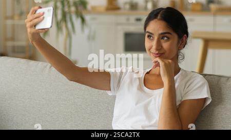 Indienne femme souriante influenceur vlogger blogueur Arabian Girl femme faire selfie photo avec téléphone portable posant canapé assis canapé à la maison smartphone Banque D'Images