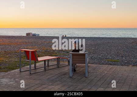 Batumi, Géorgie. 23 décembre 2013. Homme solitaire se reflète au bord de la mer pendant le coucher du soleil, chaise vide symbolisant l'absence ou la perte. Banque D'Images