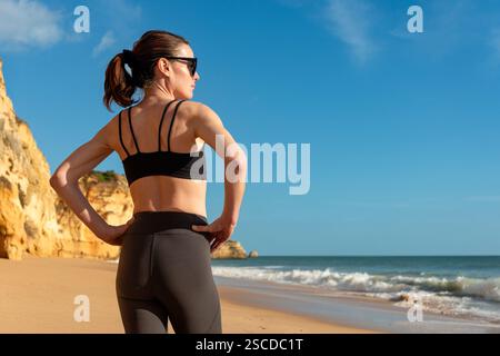 fit femme sportive debout sur la plage avec les mains sur les hanches profitant du soleil Banque D'Images