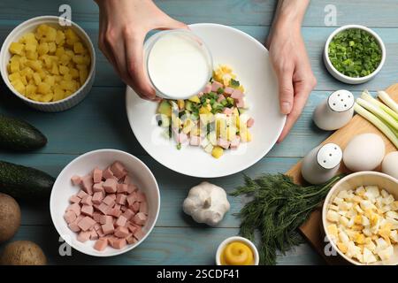 Faire de la soupe okroshka. Femme versant du kéfir dans un bol avec différents ingrédients à la table en bois bleu clair, vue de dessus Banque D'Images