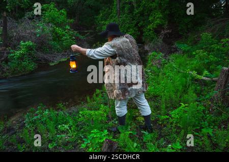 voyageur en vieux vêtements avec un sac à dos et une lampe à kérosène au croisement de la rivière Banque D'Images