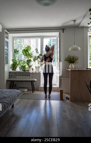 Femme focalisée sur la forme physique arrière étirer les bras dans la pose complexe de yoga, debout sur le tapis d'exercice à la maison Banque D'Images