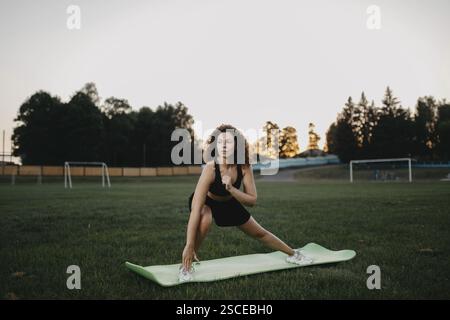 Une femme effectue un étirement latéral sur un tapis de yoga dans un parc Banque D'Images