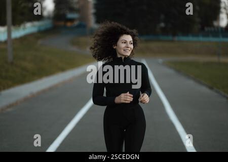 Une femme déterminée qui court sur une piste dans des vêtements sombres, montrant une concentration athlétique Banque D'Images