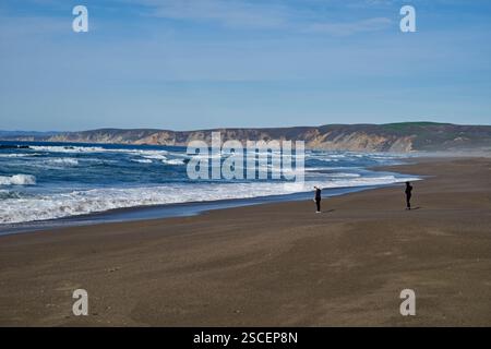 deux personnes au loin sur la plage vide avec les vagues de l'océan Banque D'Images