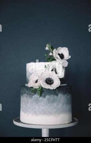 Un gâteau à deux niveaux magnifiquement conçu avec une finition grise texturée se trouve au sommet d'un présentoir à gâteaux. Fleurs blanches avec des centres sombres élégamment en cascade vers le bas d'un si Banque D'Images