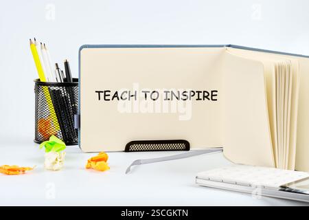 Un cahier lit Teach to inspire, entouré de papeterie colorée et de fleurs en papier, représentant un espace d'apprentissage créatif. Banque D'Images