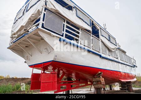 Poupe de grand bateau sur des supports en bois pour réparation sur cale sèche, avec pont supérieur couvert et garde-corps en métal, vue à angle bas contre le ciel nuageux Banque D'Images