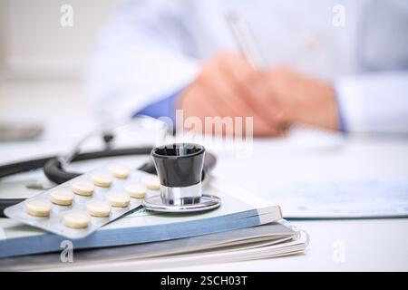 Un professionnel de la santé rédige une ordonnance à un bureau entouré d’un stéthoscope et d’un paquet de médicaments dans un environnement clinique. Banque D'Images