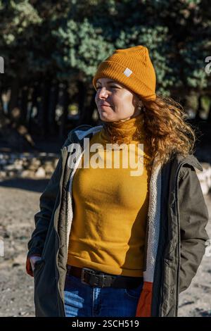 Jeune femme attrayante en bonnet orange et pull riant à l'extérieur Banque D'Images