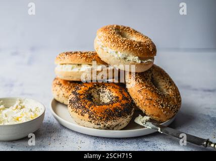Pile de bagels assortis avec du fromage à la crème sur fond clair. Banque D'Images