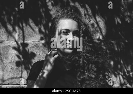 Portrait en échelle de gris Gen Z, fille souriante dans le soleil d'été et les ombres Banque D'Images