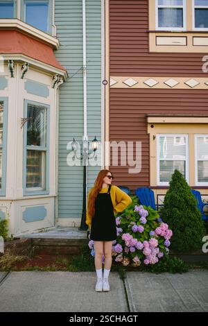 Une jeune femme aux cheveux roux se dresse à côté de l'architecture classique dans le magasin John's, Terre-Neuve-et-Labrador, Canada. Habillé dans une robe noire élégante et un Banque D'Images