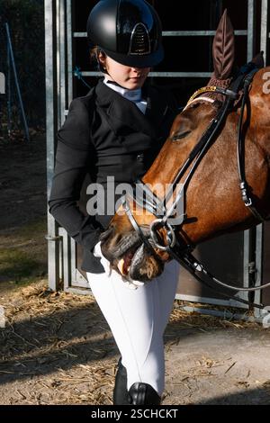 Un équestre habillé dans une tenue d'équitation formelle se tient à côté d'un cheval à l'entrée de l'écurie, symbolisant l'élégance et la discipline du classique Banque D'Images