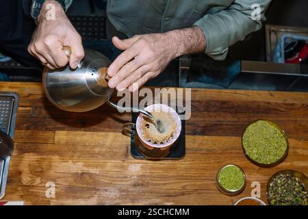Un barista verse soigneusement de l'eau sur du Marc de café dans un système de pourover, soulignant l'art de faire du café de spécialité. Les ingrédients à proximité ajoutent un coz Banque D'Images