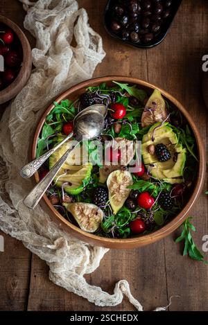 Une salade vibrante avec des figues fraîches, de l'avocat, des cerises et des mûres sur un lit de roquette, saupoudrée d'amandes dans un bol en bois, serti sur un rusti Banque D'Images