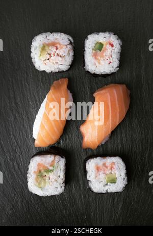 Une présentation élégante de sushis, avec des nigiri de saumon frais et des rouleaux de sushi avec du crabe, de l'avocat, du saumon et du riz, magnifiquement disposés sur un s noir Banque D'Images