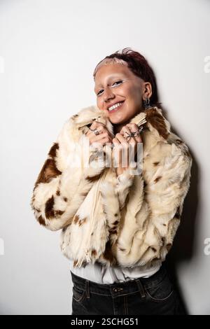 Une femme aux cheveux courts sourit chaudement à la caméra tout en portant une veste en fausse fourrure tendance. Banque D'Images