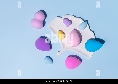 Vue de dessus de diverses éponges colorées de mélangeur de beauté et un support, artistiquement disposés sur un fond bleu clair. Idéal pour l'application de maquillage Conce Banque D'Images