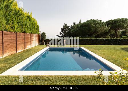 Femme pratiquant le yoga au bord d'une piscine tranquille, exécutant la pose de chameau (Ustrasana) au milieu d'une verdure sereine. Banque D'Images